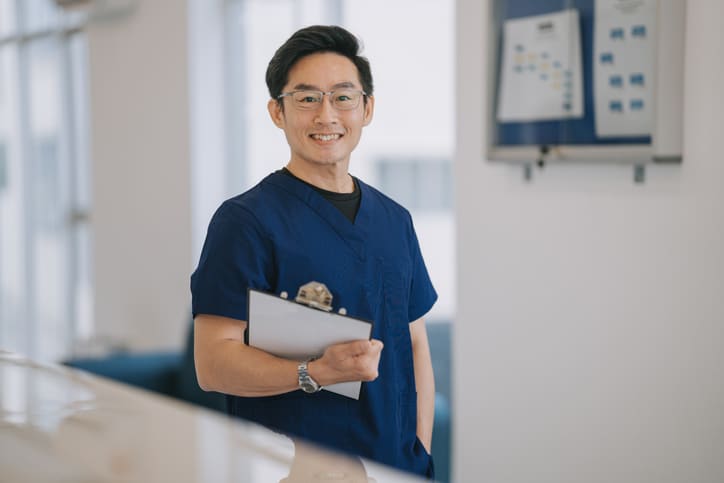 Portrait Asian male dentist holding a clipboard smiling standing in front of clinic